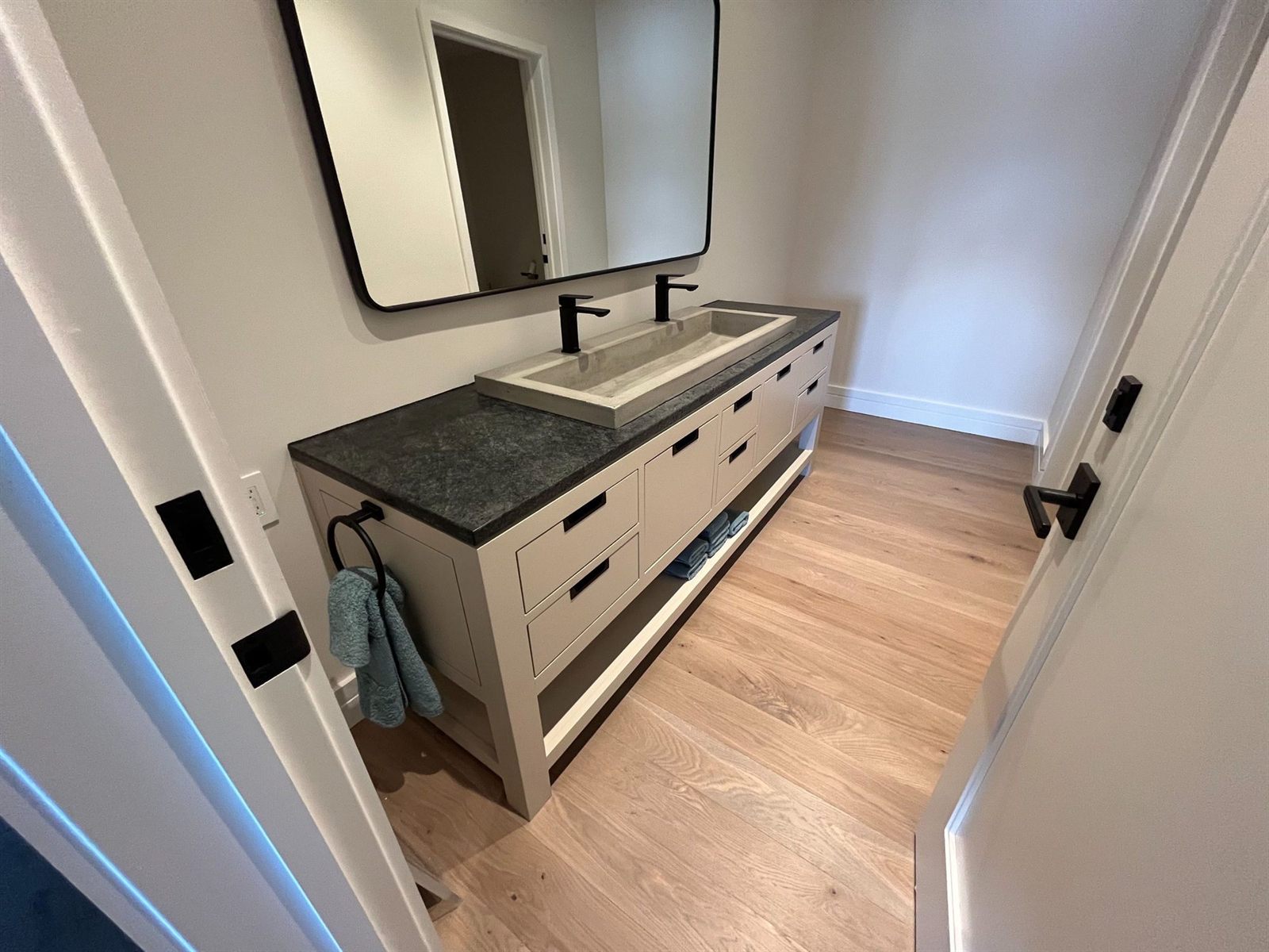 Custom double vanity with a concrete trough sink, honed stone top and open towel shelf