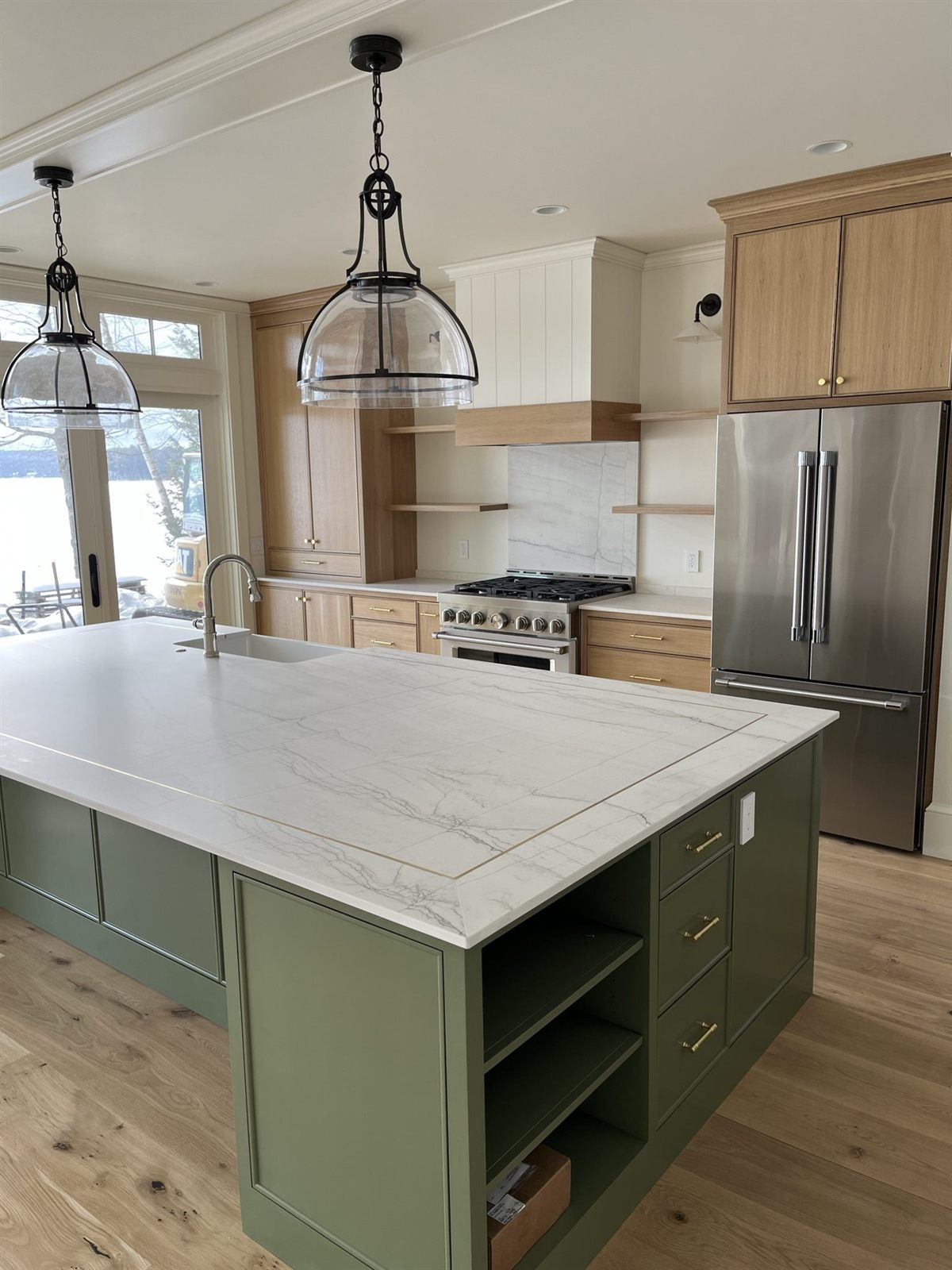 White oak kitchen cabinetry with a sage green island and brass hardware