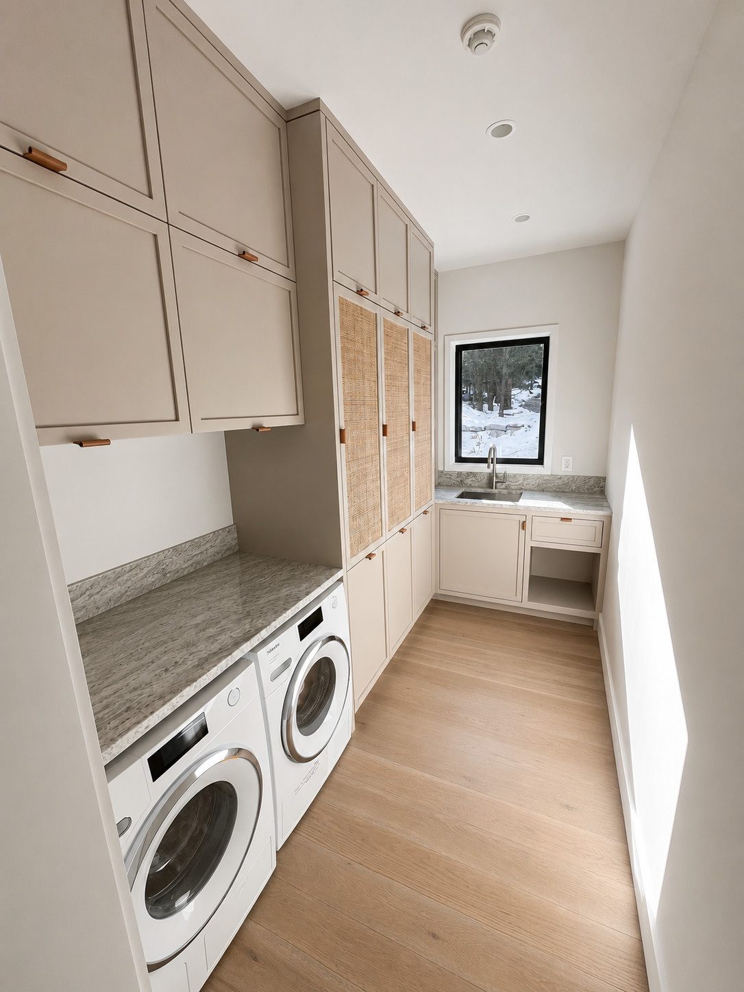 Laundry room with taupe cabinetry, cane-front doors, leather pulls and a stone folding counter
